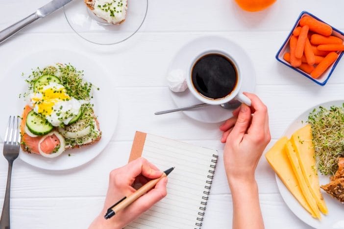 Whole30 diet concept image with notebook, coffee, and plates of food. 