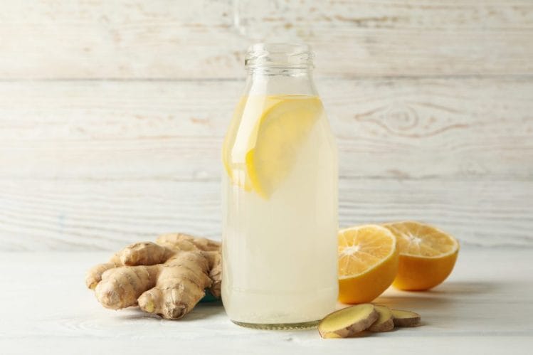 Glass of lemon water sits next to ginger and sliced oranges.