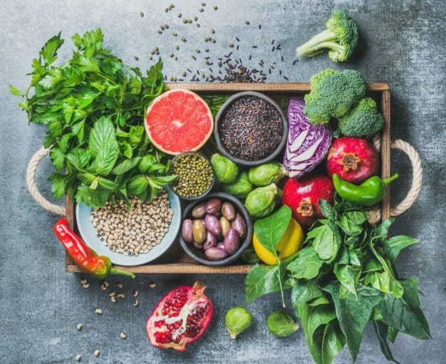 Healthy food ingredients sit in a wooden box on a grey counter.
