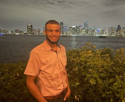 Chef Alex stands in front of Miami cityscape. 